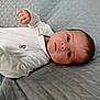 baby, infant, face, eyes, hand, onesie, white_clothing, blanket, quilted, soft_texture, lying_down, portrait, young_child, skin, head, curious, indoors, person, newborn, sleepwear
