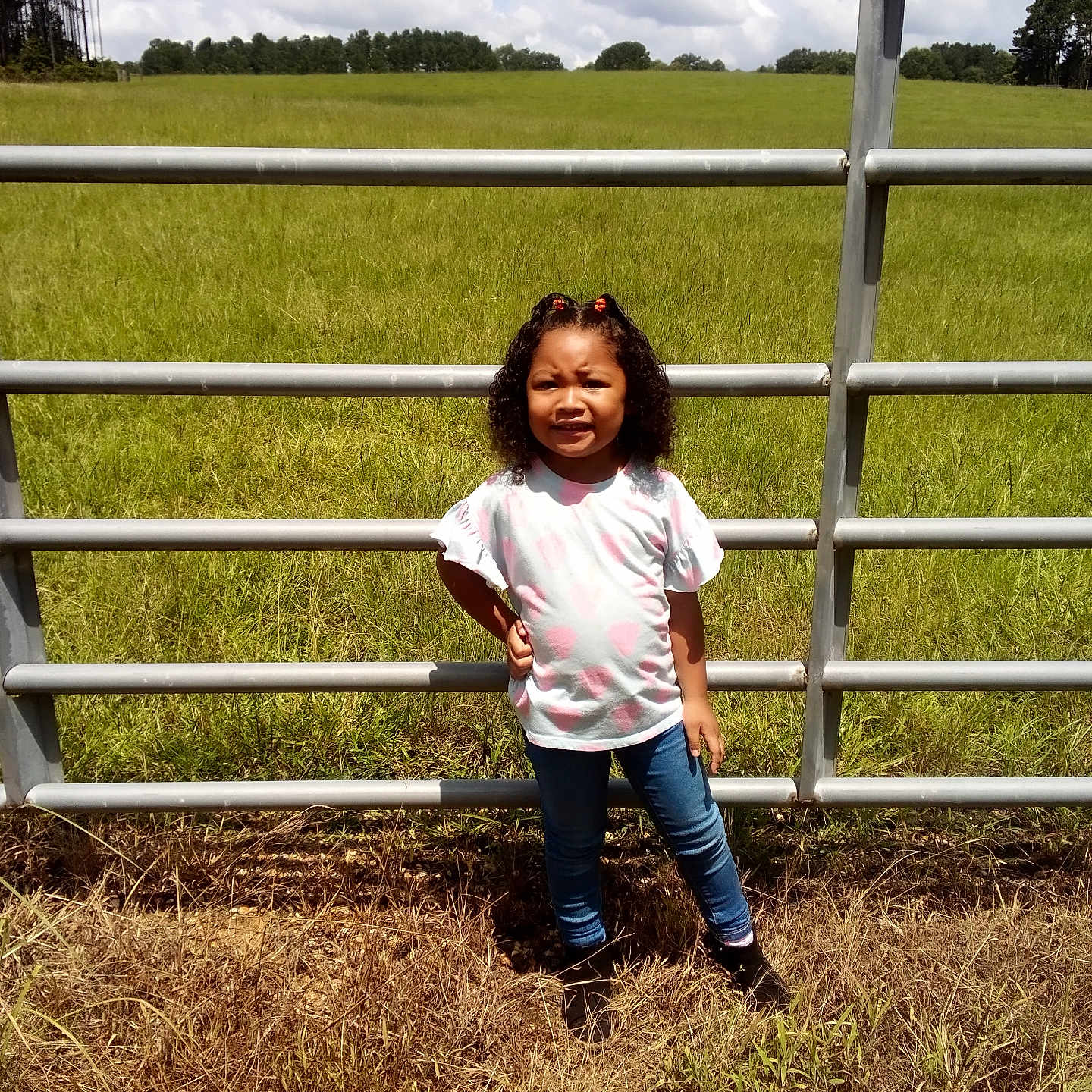 Ma'Riyah joined the competition — help win amazing prizes! boots, casual_clothing, child, clouds, curly_hair, daytime, field, girl, grass, jeans, metal_fence, nature, outdoor, portrait, rural, sky, standing, sunny, trees, white_shirt