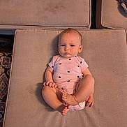 Sabrina is registered to the contest to win money with this photo: baby, infant, child, onesie, pink_clothing, polka_dots, cushion, beige, face, feet, legs, arm, hand, expression, indoor, carpet, fabric, soft, person, cute