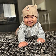 Juan is registered to the contest to win money with this photo: baby, child, smiling, beanie, hat, indoor, carpet, floor, cute, happy, infant, person, clothing, portrait, headwear, toddler, home, cozy, furniture, expression