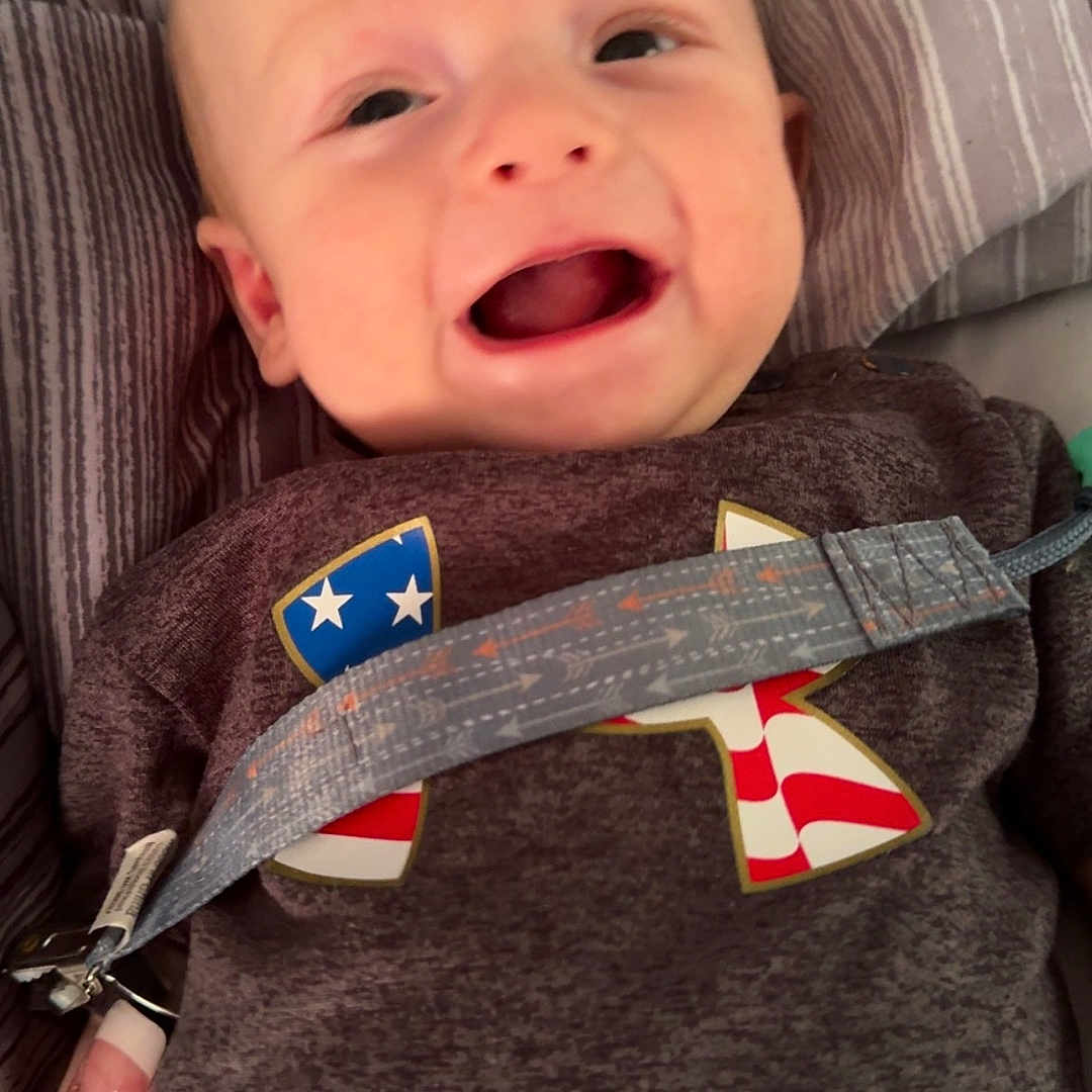 Jaxton is registered to the contest to win money with this photo: accessories, baby, belt, bodypart, clothing, couch, cushion, face, finger, furniture, hand, happy, head, homedecor, pants, person, photography, portrait, strap, t_shirt