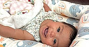 Serena is registered to the contest to win money with this photo: baby, smiling, infant, blanket, cushion, elephant_pattern, rainbow_pattern, baby_bed, pink, white, soft_toys, indoor, happy, face, child, resting, cozy, cute, person, nursery