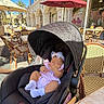 baby, stroller, outdoor, cafe, umbrella, child, infant, sunlight, table, chair, building, window, footwear, headband, relaxing, shade, people, daylight, person, fashion