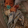 baby, pacifier, blanket, plush_toy, pajamas, baby_seat, infant, cute, soft_toy, cushion, sleepwear, child, indoors, footwear, animal_print, comfort, resting, baby_clothes, small_hands, warm_lighting