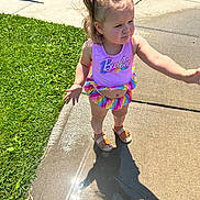 Charli joined the competition — help win amazing prizes! barbie, child, curly_hair, daylight, expression, footwear, gesture, grass, hair, outdoor, playful, sandals, shadow, sidewalk, summer, sunlight, swimsuit, toddler, water, wet_surface
