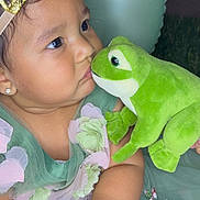 Marbella joined the competition — help win amazing prizes! adorable, baby, child, closeup, crown, curious, cute, dress, earrings, face, flower, frog, green_dress, hands, indoors, plush_toy, portrait, soft_toy, toddler, toy