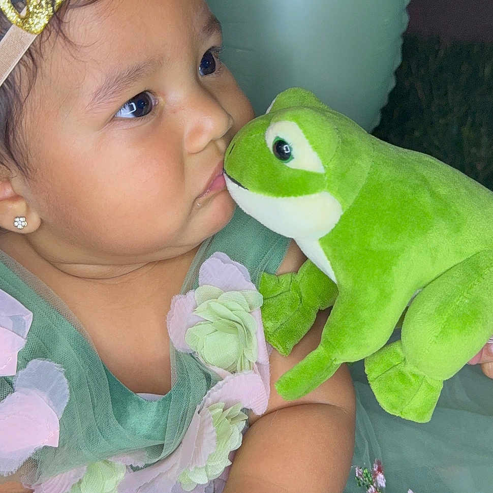 Marbella joined the competition — help win amazing prizes! adorable, baby, child, closeup, crown, curious, cute, dress, earrings, face, flower, frog, green_dress, hands, indoors, plush_toy, portrait, soft_toy, toddler, toy