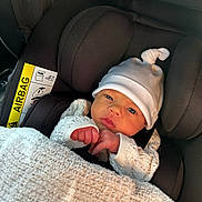 Mabel joined the competition — help win amazing prizes! baby, newborn, car_seat, blanket, hat, infant, child, knitted_sweater, seatbelt, indoors, cute, portrait, warm, cozy, face, headwear, sitting, small_hands, car_interior, soft_lighting