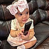 baby, bow, bracelet, child, clothing, couch, curious, cute, furniture, headband, indoors, leather, person, pink, remote_control, sitting, small_hands, socks, toddler, white