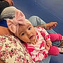 Valentina a rejoint le concours — aidez-le/la à gagner de superbes lots ! baby, child, pink_bow, headband, floral_shirt, lap, indoor, bleachers, curious, casual_clothing, person, seated, jeans, tattoo, watch, footwear, socks, cute, portrait, young_child