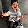 Valentina participe au concours pour gagner de l'argent avec cette photo : baby, child, smiling, couch, remote_control, socks, turban, bow, sweater_vest, striped_clothing, happy, indoor, person, seated, furniture, home, cozy, cute, hands, feet