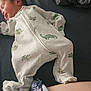 newborn, baby, sleeping, onesie, dinosaur_pattern, bed, blanket, clothing, infant, fabric, floral_pattern, peaceful, resting, cute, young_child, portrait, soft_lighting, indoors, closeup, toddler