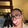 black_cat, casual_clothing, cat, curious, earrings, face_occluded, glasses, home, indoor, jewelry, kitten, necklace, person, pet, portrait, ring, shoulder, stairs, warm_lighting, wooden_stairs