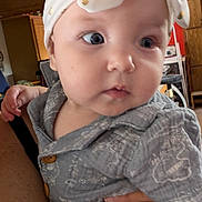 Blair joined the competition — help win amazing prizes! baby, infant, child, portrait, close_up, wide_eyes, headband, gray_outfit, clothing, sitting, held, adult_hand, indoor, home, wood_cabinet, furniture, warm_lighting, candid, face, photography