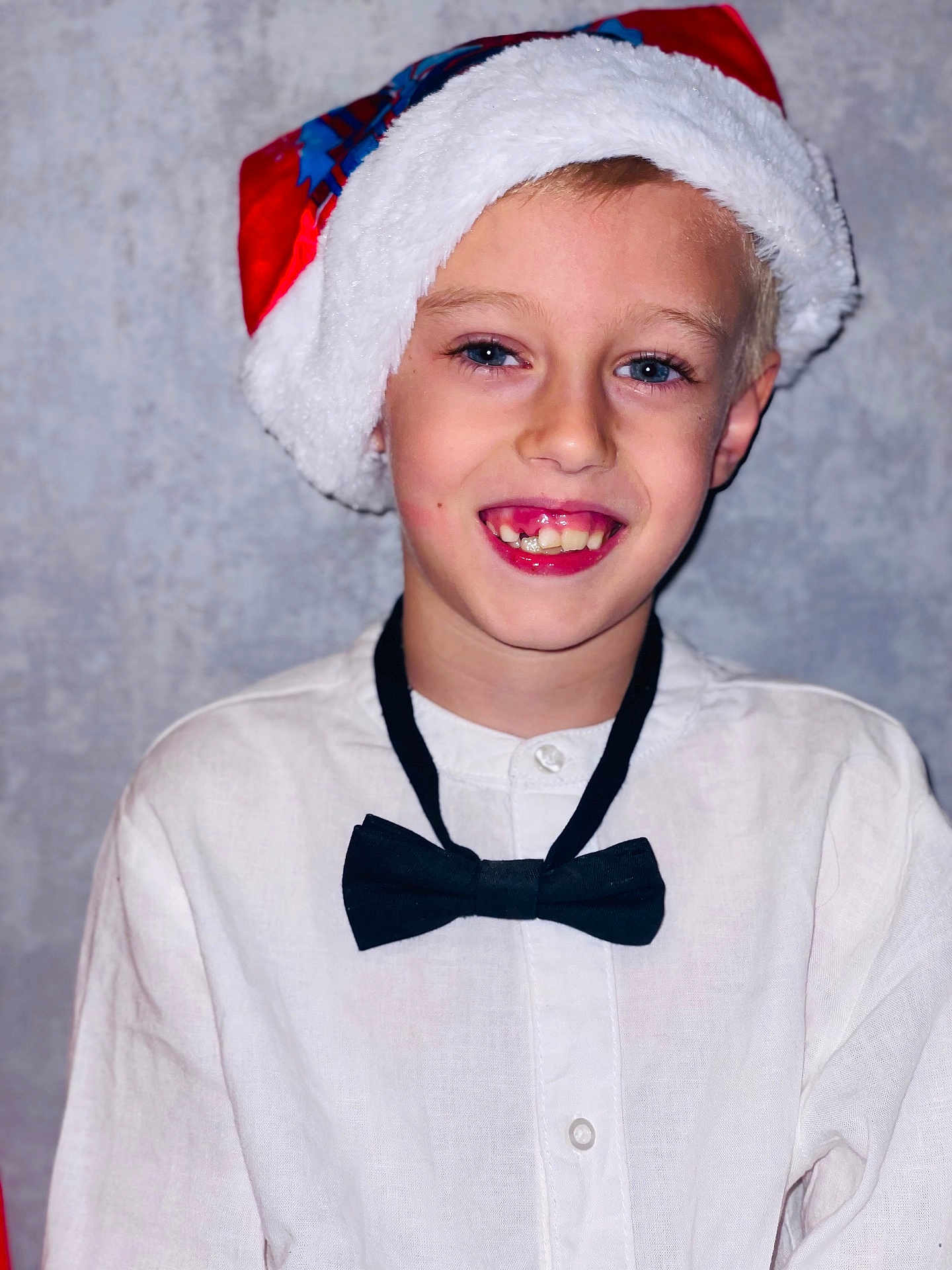 Théo participe au concours pour gagner de l'argent avec cette photo : child, boy, smile, santa_hat, bow_tie, white_shirt, portrait, face, holiday, festive, young, person, blue_eyes, happy, indoor, casual, cute, closeup, celebration, background