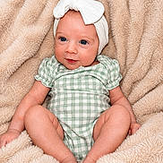 Mckenna is registered to the contest to win money with this photo: baby, infant, headband, bow, green_checkered, blanket, soft_texture, cute, portrait, child, smiling, sitting, skin, face, newborn, comfortable, relaxed, indoor, clothing, young