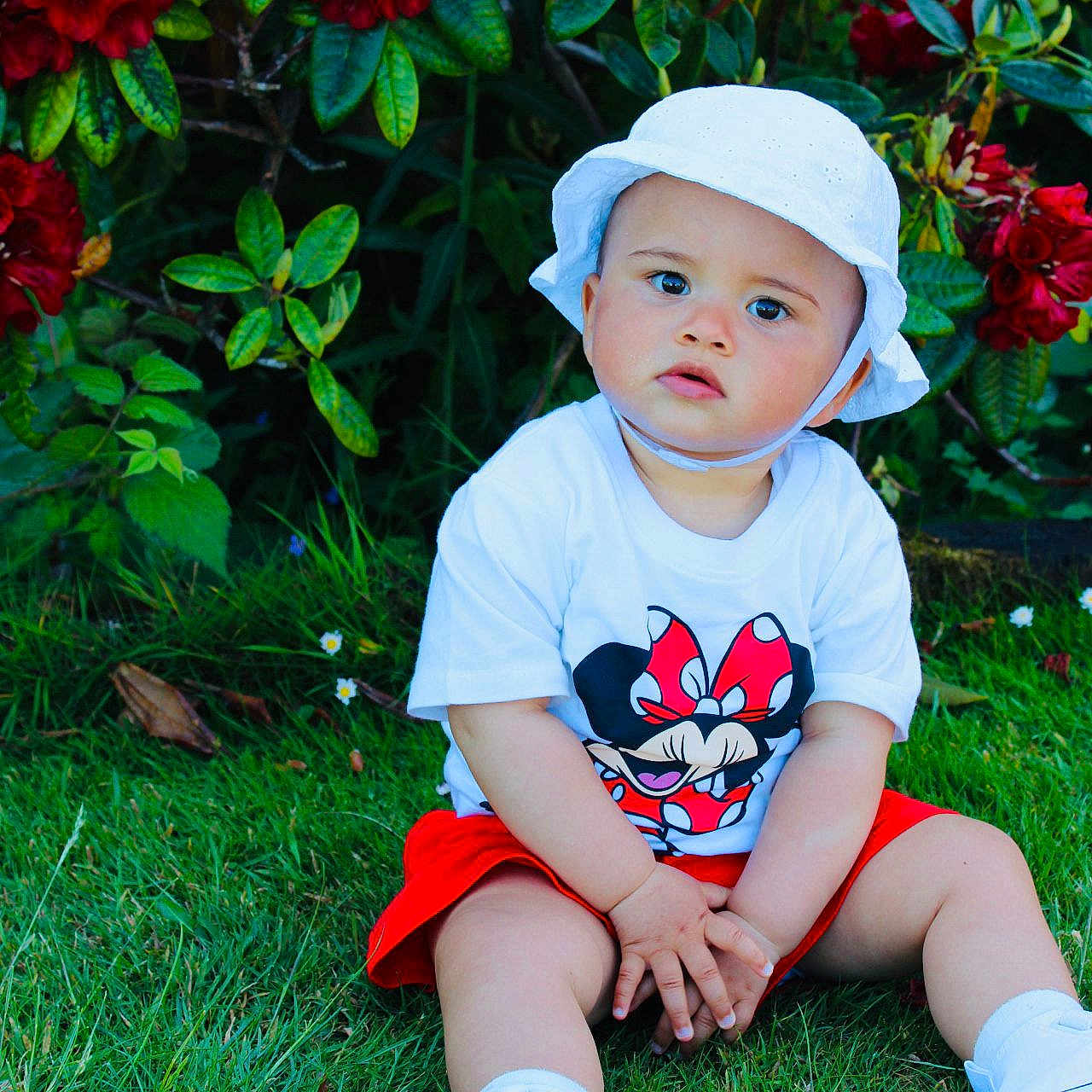 Zara is registered to the contest to win money with this photo: baby, cap, clothing, face, flower, footwear, grass, hat, head, lawn, leaf, person, photography, plant, portrait, shoe, shorts, sitting, sneaker, sunhat