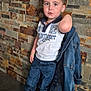 child, boy, denim_jacket, white_shirt, jeans, sneakers, stone_wall, bracelet, floor, standing, casual, portrait, indoor, fashion, cute, young, person, footwear, clothing, posing