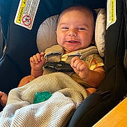 Grayson is registered to the contest to win money with this photo: baby, car_seat, chicco, blanket, pacifier, smiling, infant, child, safety_harness, indoor, cute, happy, clothing, warning_label, seat, person, portrait, small_hands, baby_girl, baby_boy