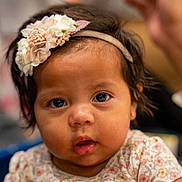 Mayorga joined the competition — help win amazing prizes! baby, child, face, headband, flower, hand, person, portrait, cute, infant, skin, clothing, floral, expression, looking, young, indoors, soft_focus, holding, curious