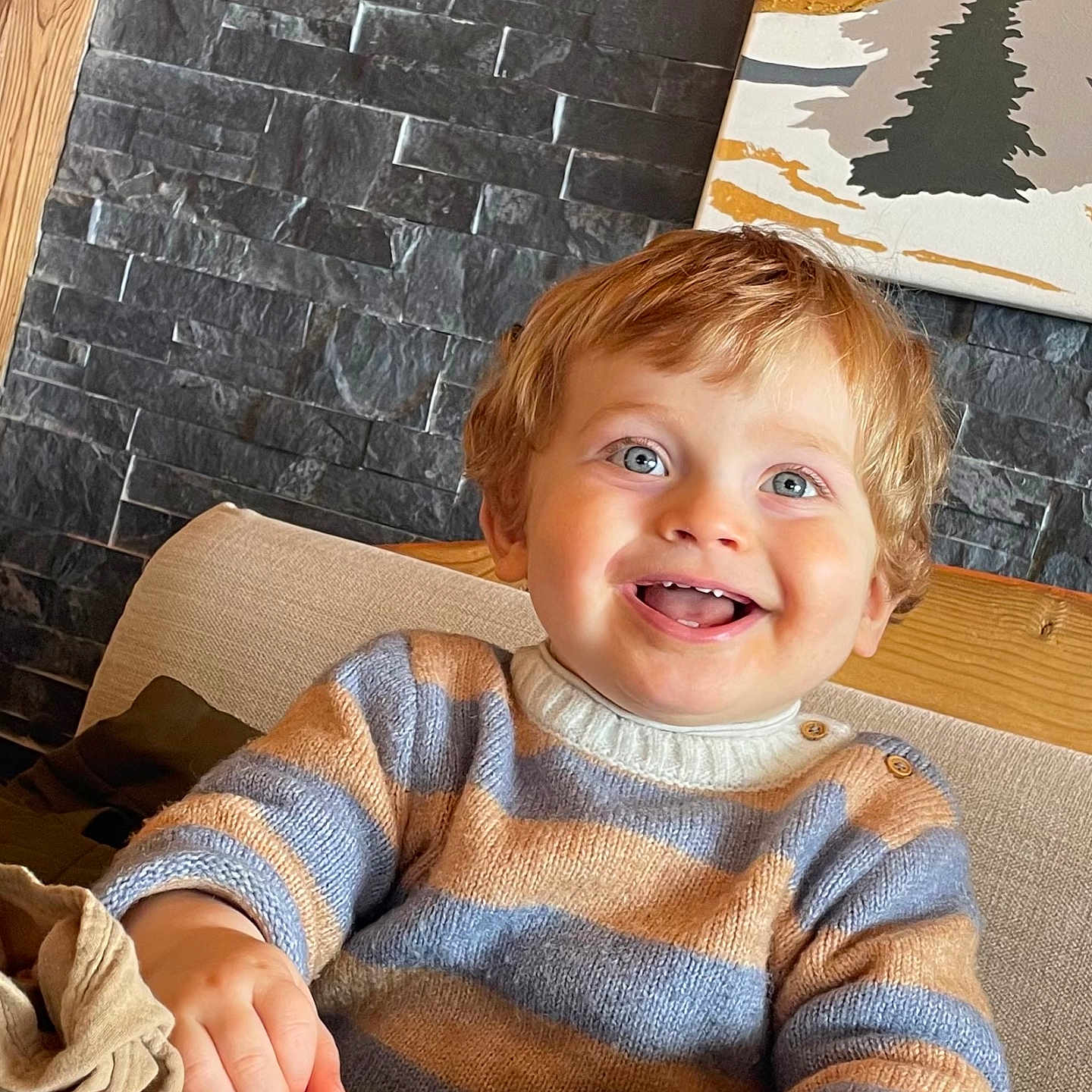 Owen participe au concours pour gagner de l'argent avec cette photo : blue_eyes, bright, casual_clothing, child, couch, cozy, cute, happy, indoor, menu, person, portrait, seated, smiling, stone_wall, striped_sweater, table, toddler, wood, young_child
