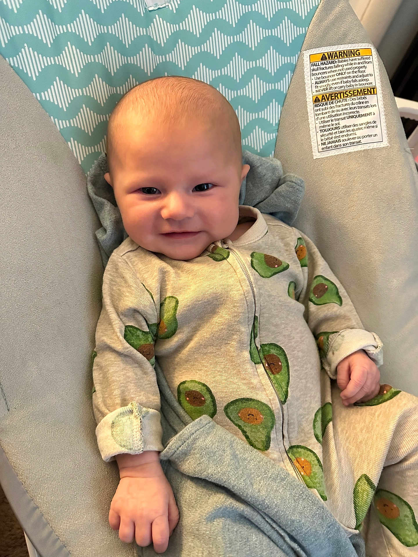 Ames is registered to the contest to win money with this photo: baby, infant, onesie, avocado_pattern, smile, face, hand, baby_seat, blanket, fabric, comfort, cute, child, indoor, portrait, clothing, sitting, relaxed, young, soft