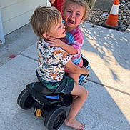Kathleen is registered to the contest to win money with this photo: child, boy, girl, toy_vehicle, outdoor, concrete, crying, red_shirt, shorts, barefoot, greenery, traffic_cone, sunlight, sidewalk, rock, playing, emotion, summer, daylight, expression