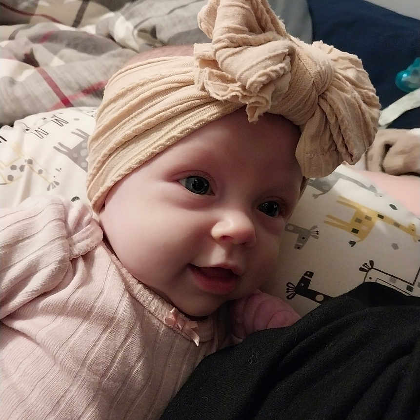 Ellen is registered to the contest to win money with this photo: baby, blanket, bow, child, clothing, cozy, cute, face, happy, headwrap, indoors, infant, newborn, pattern, person, pillow, portrait, resting, smile, soft