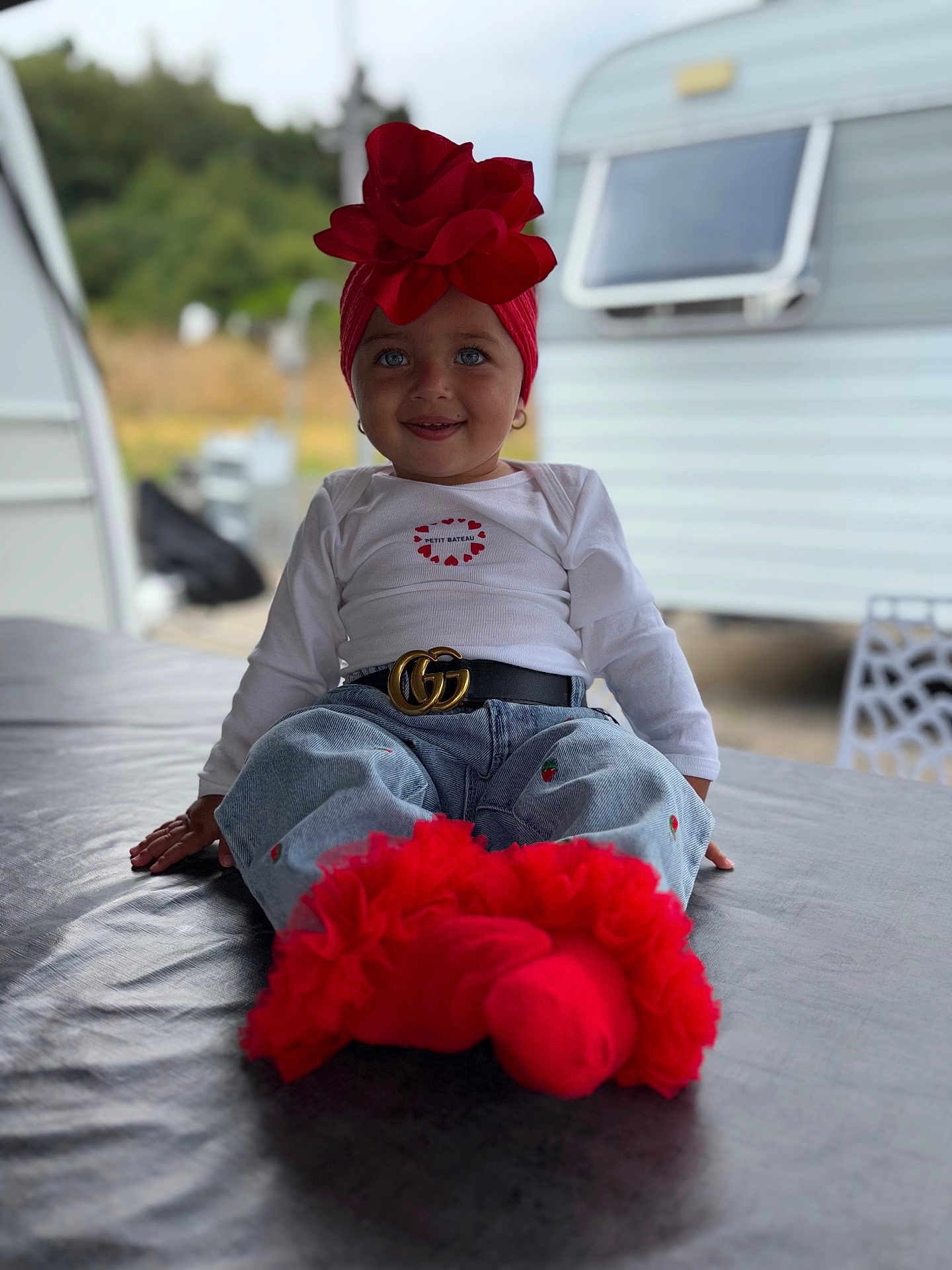 Eva participe au concours pour gagner de l'argent avec cette photo : toddler, child, red_headwrap, flower, blue_eyes, white_shirt, jeans, belt, red_socks, frills, sitting, outdoor, caravan, smiling, portrait, fashion, casual, cute, happy, person