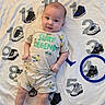 baby, infant, child, cute, smiling, clothing, tshirt, shorts, lying_down, blanket, numbers, sneakers, cartoon, pattern, playful, indoors, portrait, person, happy, bright