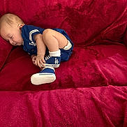 Jesse joined the competition — help win amazing prizes! baby, sleeping, blue_clothing, couch, red_fabric, infant, footwear, socks, indoors, child, resting, cute, soft_texture, relaxed, small, person, portrait, cozy, casual, home