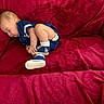 baby, sleeping, blue_clothing, couch, red_fabric, infant, footwear, socks, indoors, child, resting, cute, soft_texture, relaxed, small, person, portrait, cozy, casual, home