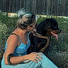 woman, dog, rottweiler, outdoor, fence, grass, casual_clothing, sitting, leash, pet, animal, blonde_hair, activewear, side_view, tongue_out, nature, social_media, text_overlay, promotion, happy