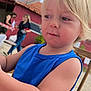 Juan participe au concours pour gagner de l'argent avec cette photo : toddler, child, blonde_hair, blue_clothing, tank_top, table, checkered_tablecloth, outdoor, umbrella, people, adult, background, curious_expression, daylight, seat, wooden_chair, person, summer, casual, portrait