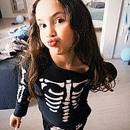 Chloe participe au concours pour gagner de l'argent avec cette photo : child, skeleton_costume, face, indoor, playful, puckered_lips, long_hair, messy_background, balloon, clothing, person, casual, home, floor, mirror, bed, toy, pose, cute, fashion