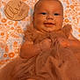 baby, smiling, dress, blanket, floral_pattern, plaque, name, infant, cute, lying_down, face, hands, legs, soft_fabric, cozy, child, portrait, happy, indoors, newborn