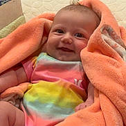 Amelia joined the competition — help win amazing prizes! baby, infant, blanket, orange_blanket, colorful_clothing, tie_dye, smiling, happy, cute, face, indoors, soft_texture, cushion, floor, wooden_floor, child, person, young_child, comfortable, cozy