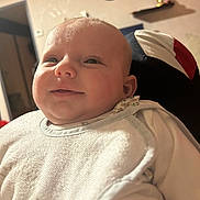 Elyana a rejoint le concours — aidez-le/la à gagner de superbes lots ! baby, smile, face, infant, clothing, indoor, bib, person, cute, portrait, child, head, soft_light, happy, young, home, sitting, warm, cozy, background