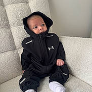 Cruz is registered to the contest to win money with this photo: baby, black_clothing, casual_wear, chair, child, comfortable, cozy, curious_expression, cute, furniture, hoodie, indoor, infant, looking_away, person, portrait, seated, socks, soft_texture, young