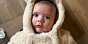 Cruz is registered to the contest to win money with this photo: baby, babywear, bundle, child, clothing, coat, cute, expression, eyes, face, floor, fur, hood, indoors, infant, person, portrait, soft, warm, wood