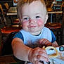 Braxton is registered to the contest to win money with this photo: baby, child, high_chair, bib, food, curly_fry, smile, rosy_cheeks, restaurant, table, chair, adult, indoor, lighting, face, hand, clothing, person, happy, dining