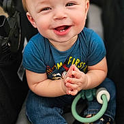 Braxton is registered to the contest to win money with this photo: baby, child, smiling, stroller, blue_shirt, jeans, boots, hands, face, happy, cute, toy, socks, indoor, portrait, infant, person, clothing, footwear, expression