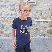 Noah a rejoint le concours — aidez-le/la à gagner de superbes lots ! child, boy, glasses, smiling, tshirt, shorts, sandals, stone_wall, pavement, window, outdoor, person, casual_clothing, summer, happy, standing, young, portrait, fashion, daylight