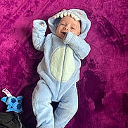 Emilio a rejoint le concours — aidez-le/la à gagner de superbes lots ! baby, baby_toy, blue_clothing, child, cozy, cute, face, hand_near_mouth, happy, hood, indoor, infant, lying_down, onesie, plush_toy, portrait, purple_blanket, smile, soft_texture, warm_clothing