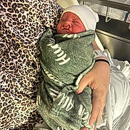 Hudson is registered to the contest to win money with this photo: baby, bed, blanket, care, closeup, hands, hospital, hospital_bassinet, indoor, infant, leopard_print, maternity, newborn, parent, person, resting, sleeping, swaddled, white_hat, wristband