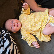 Isabelle joined the competition — help win amazing prizes! baby, infant, yellow_dress, smiling, couch, blanket, zebra_pattern, arm, socks, happy, person, child, indoor, relaxing, clothing, fabric, skin, portrait, cute, lying_down