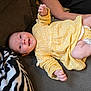baby, infant, yellow_dress, smiling, couch, blanket, zebra_pattern, arm, socks, happy, person, child, indoor, relaxing, clothing, fabric, skin, portrait, cute, lying_down