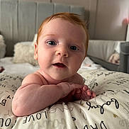 Willow is registered to the contest to win money with this photo: baby, infant, red_hair, face, eyes, skin, pillow, text, bedroom, blanket, furniture, indoor, child, curious, closeup, portrait, hands, expression, home, soft