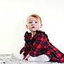 baby, child, red_hair, blue_eyes, plaid_dress, bow, sitting, white_background, fluffy_rug, soft_texture, cute, portrait, innocent_expression, long_sleeves, toddler, studio_photo, cozy, young_child, holiday_style, fashion