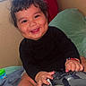 baby, child, smiling, controller, video_game, indoor, bed, blanket, red_curtain, window, black_clothing, bracelet, foot, happy, person, cute, dim_light, playing, toy, room